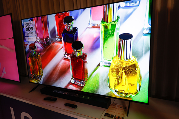 מסך טלוויזיה גדול המציג בקבוקי זכוכית צבעוניים עם תאורה אחורית. בר קול ממוקם מתחת לטלוויזיה, וילונות נראים ברקע.