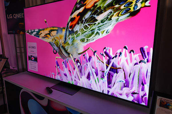 מסך טלוויזיה גדול המציג תמונת תקריב של פרפר על רקע ורוד. הטלוויזיה מסומנת בתווית "LG QNED.